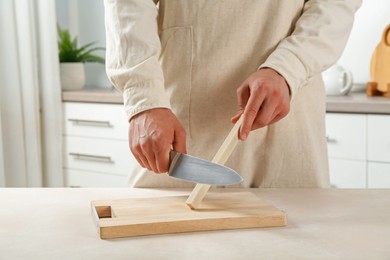 Photo of Man sharpening knife with sharpener at beige table indoors, closeup