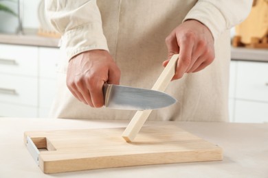 Photo of Man sharpening knife with sharpener at beige table indoors, closeup