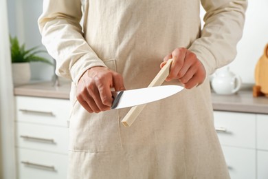 Photo of Man sharpening knife with sharpener indoors, closeup