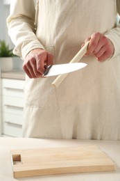 Photo of Man sharpening knife with sharpener at beige table indoors, closeup