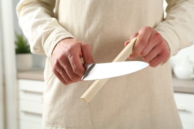 Photo of Man sharpening knife with sharpener indoors, closeup