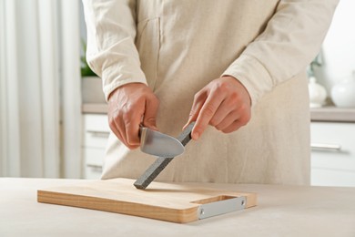 Photo of Man sharpening knife with sharpener at beige table indoors, closeup