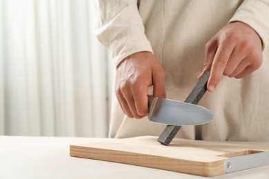 Photo of Man sharpening knife with sharpener at beige table indoors, closeup. Space for text