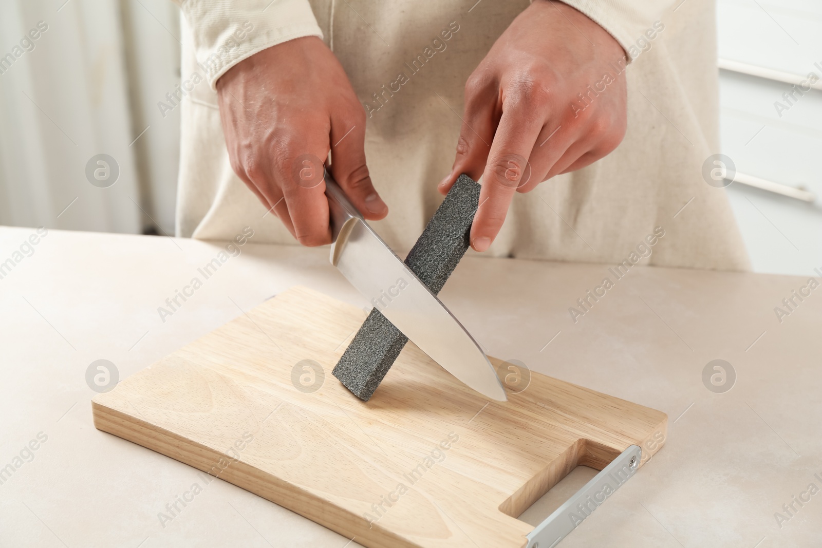 Man sharpening knife with sharpener at beige table indoors, closeup Photo of Man sharpening knife with sharpener at beige table indoors, closeup