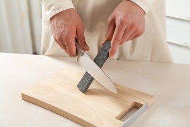 Photo of Man sharpening knife with sharpener at beige table indoors, closeup