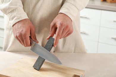 Photo of Man sharpening knife with sharpener at beige table indoors, closeup