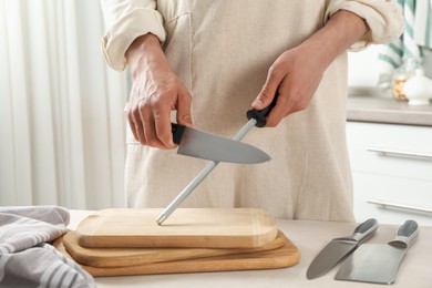 Photo of Man sharpening knife with sharpener at beige table indoors, closeup