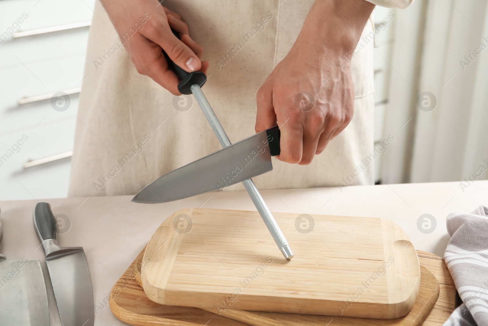 Man sharpening knife with sharpener at beige table indoors, closeup Photo of Man sharpening knife with sharpener at beige table indoors, closeup