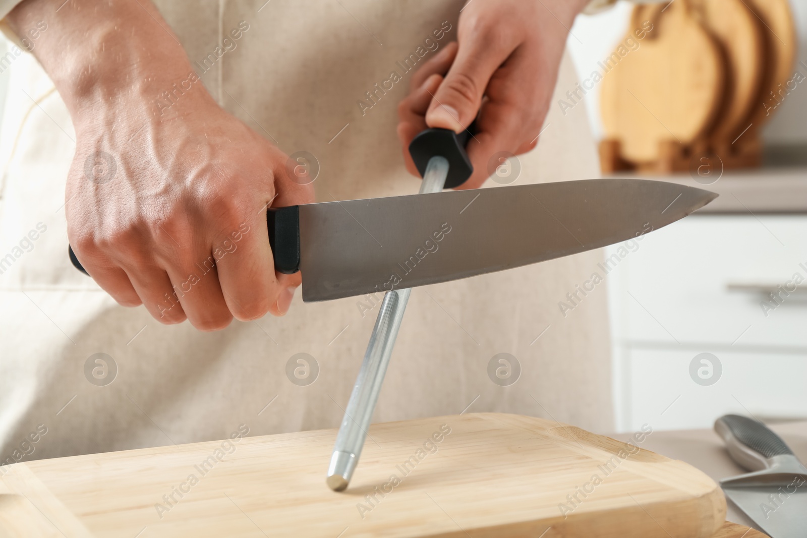 Man sharpening knife with sharpener at table indoors, closeup Photo of Man sharpening knife with sharpener at table indoors, closeup