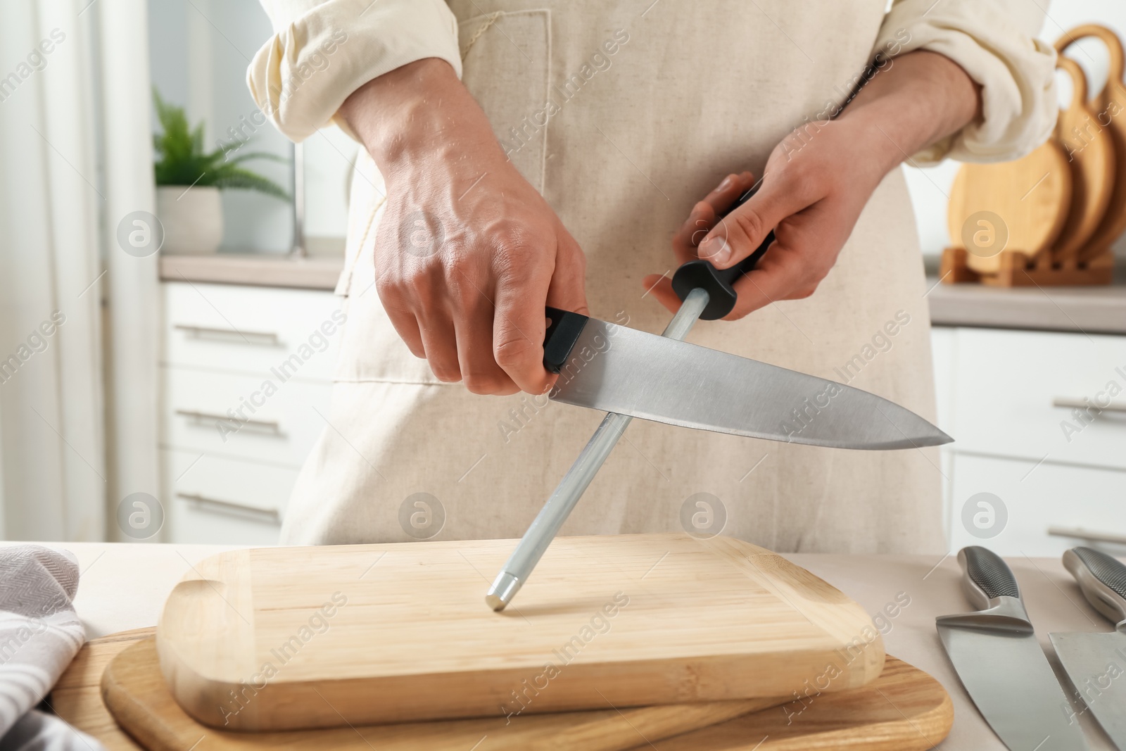 Man sharpening knife with sharpener at beige table indoors, closeup Photo of Man sharpening knife with sharpener at beige table indoors, closeup