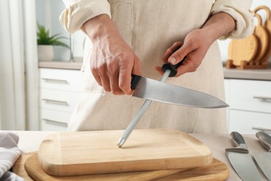 Photo of Man sharpening knife with sharpener at beige table indoors, closeup