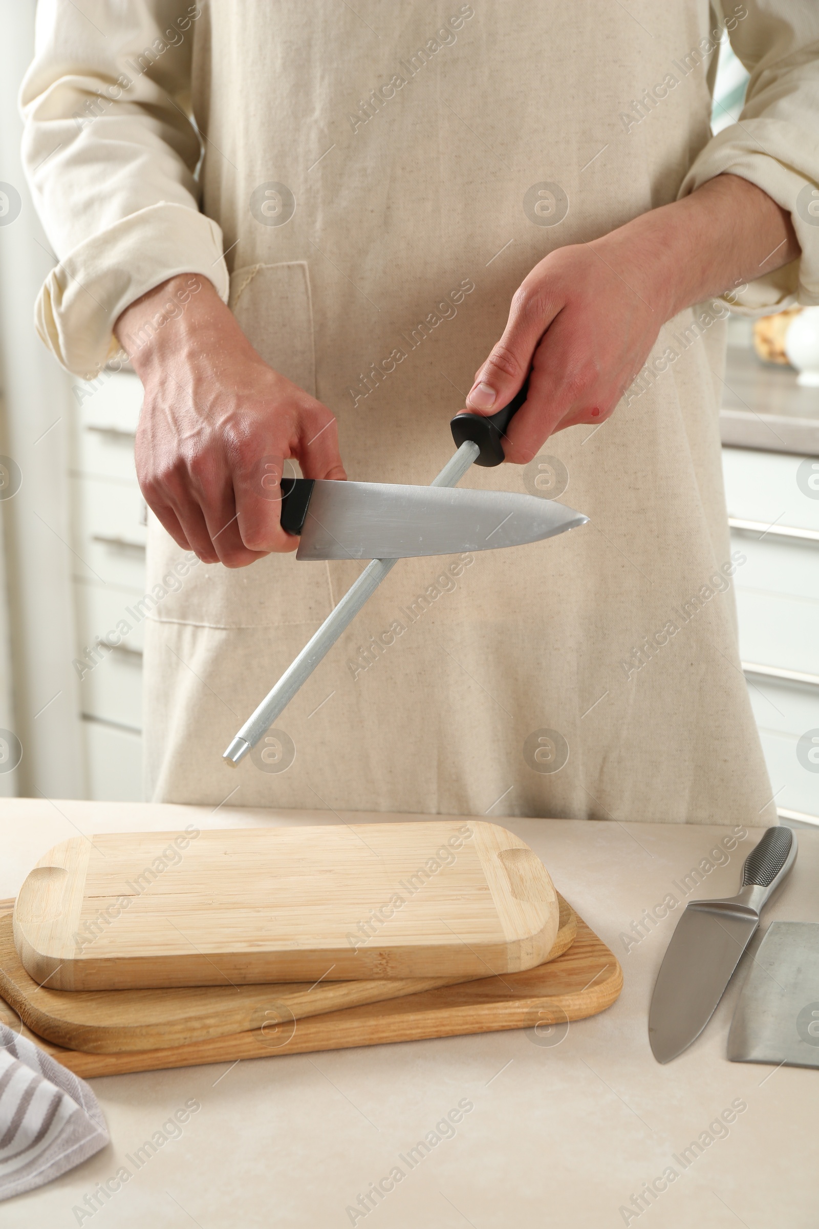 Man sharpening knife with sharpener at beige table indoors, closeup Photo of Man sharpening knife with sharpener at beige table indoors, closeup