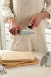 Photo of Man sharpening knife with sharpener at beige table indoors, closeup