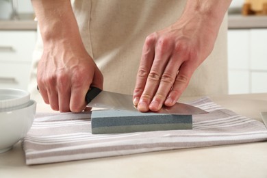 Photo of Man sharpening knife with sharpener at beige table indoors, closeup
