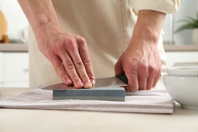 Photo of Man sharpening knife with sharpener at beige table indoors, closeup