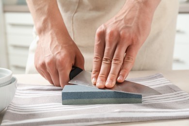 Photo of Man sharpening knife with sharpener at beige table indoors, closeup