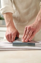 Photo of Man sharpening knife with sharpener at beige table indoors, closeup