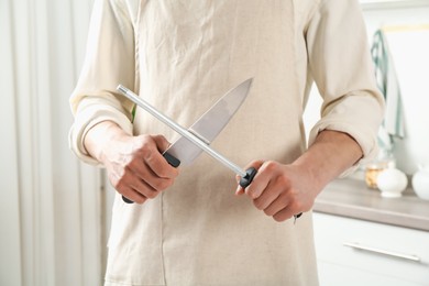 Photo of Man sharpening knife with sharpener indoors, closeup