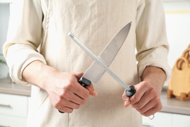 Photo of Man sharpening knife with sharpener indoors, closeup