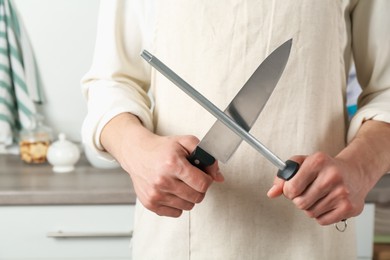 Photo of Man sharpening knife with sharpener indoors, closeup