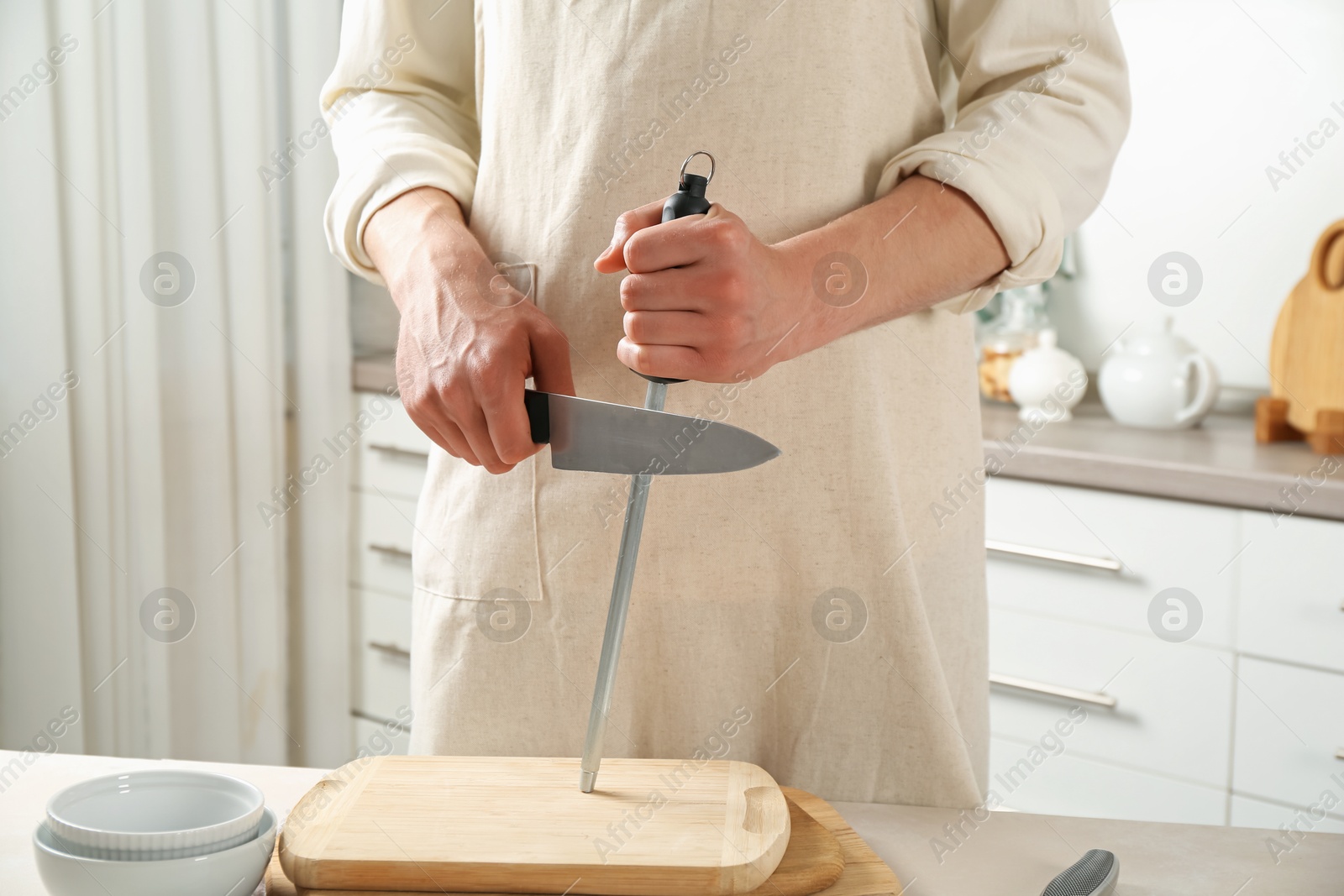 Man sharpening knife with sharpener at beige table indoors, closeup Photo of Man sharpening knife with sharpener at beige table indoors, closeup
