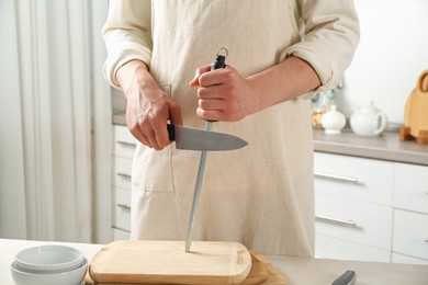 Photo of Man sharpening knife with sharpener at beige table indoors, closeup