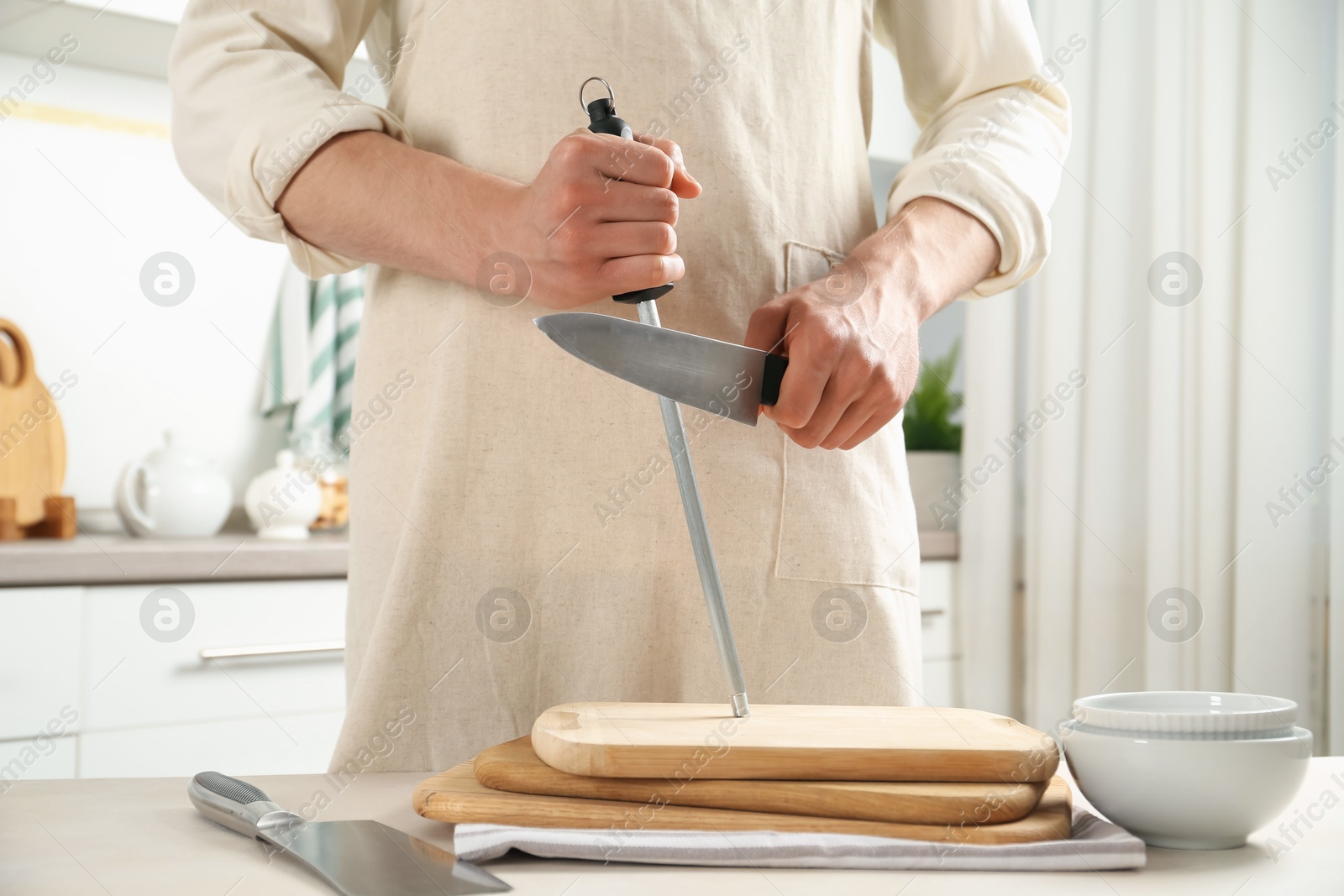 Man sharpening knife with sharpener at beige table indoors, closeup Photo of Man sharpening knife with sharpener at beige table indoors, closeup