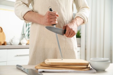 Photo of Man sharpening knife with sharpener at beige table indoors, closeup