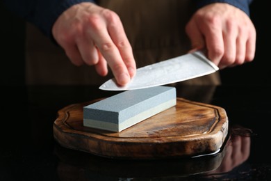 Photo of Man sharpening knife with sharpener at mirror table, closeup