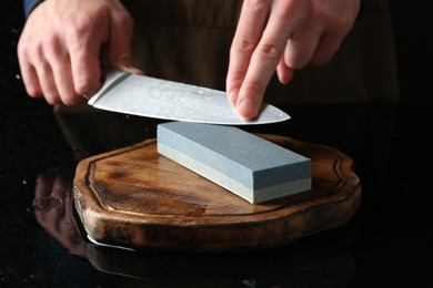 Photo of Man sharpening knife with sharpener at mirror table, closeup