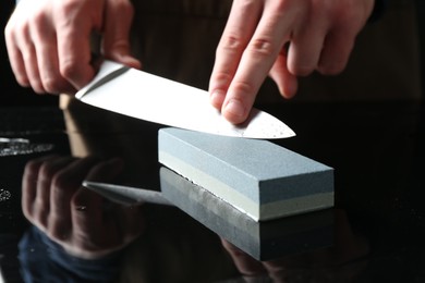 Photo of Man sharpening knife with sharpener at mirror table, closeup
