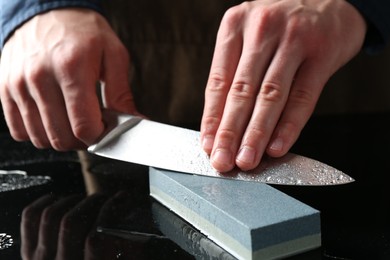 Photo of Man sharpening knife with sharpener at mirror table, closeup
