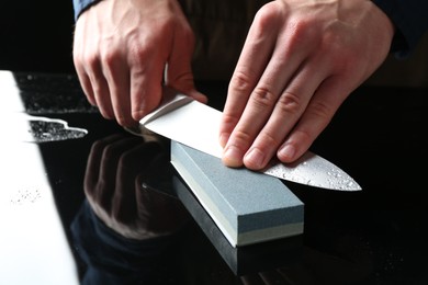 Photo of Man sharpening knife with sharpener at mirror table, closeup