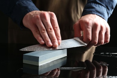 Photo of Man sharpening knife with sharpener at mirror table, closeup