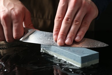Photo of Man sharpening knife with sharpener at mirror table, closeup