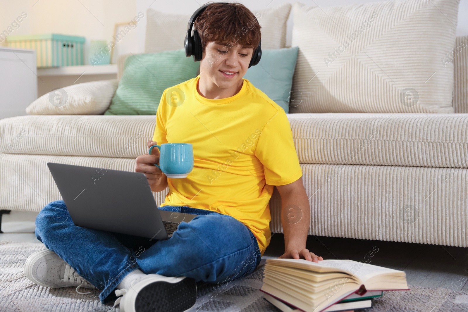 Teenage student with cup of drink and laptop studying on floor at home Photo of Teenage student with cup of drink and laptop studying on floor at home