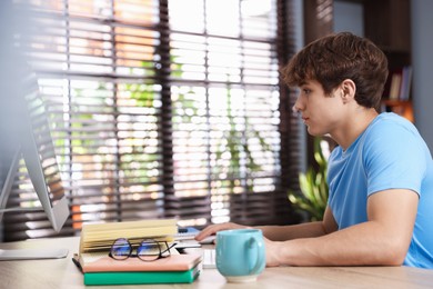 Photo of Teenage student using computer while studying at table indoors
