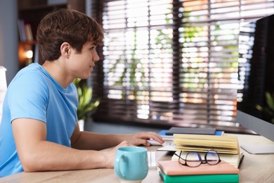 Photo of Teenage student using computer while studying at table indoors