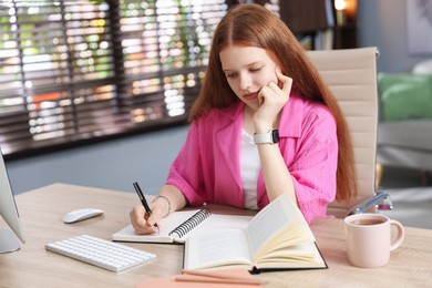 Photo of Teenage student taking notes while studying at table indoors