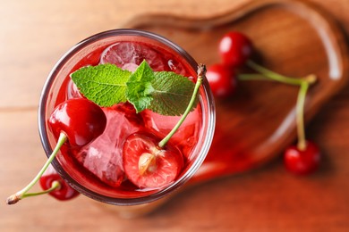 Photo of Tasty cherry soda water with ice cubes, berries and mint in glass on table, top view