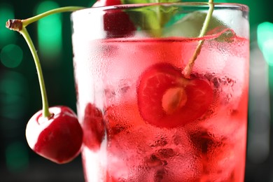 Photo of Tasty cherry soda water with ice cubes, berries and mint in glass on blurred green background, closeup