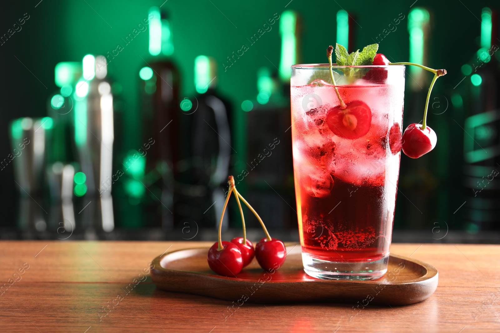 Tasty cherry soda water with ice cubes, berries and mint in glass on table against blurred green background, space for text Photo of Tasty cherry soda water with ice cubes, berries and mint in glass on table against blurred green background, space for text