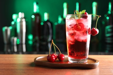 Photo of Tasty cherry soda water with ice cubes, berries and mint in glass on table against blurred green background, space for text