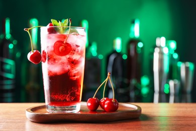 Photo of Tasty cherry soda water with ice cubes, berries and mint in glass on table against blurred green background, space for text
