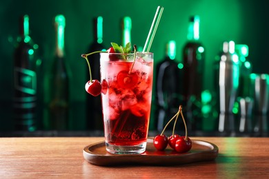 Photo of Tasty cherry soda water with ice cubes, berries and mint in glass on table against blurred green background