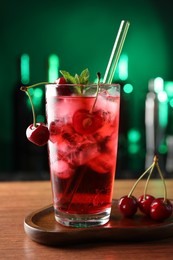Photo of Tasty cherry soda water with ice cubes, berries and mint in glass on table against blurred green background, closeup