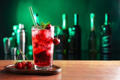 Photo of Tasty cherry soda water with ice cubes, berries and mint in glass on table against blurred green background, space for text