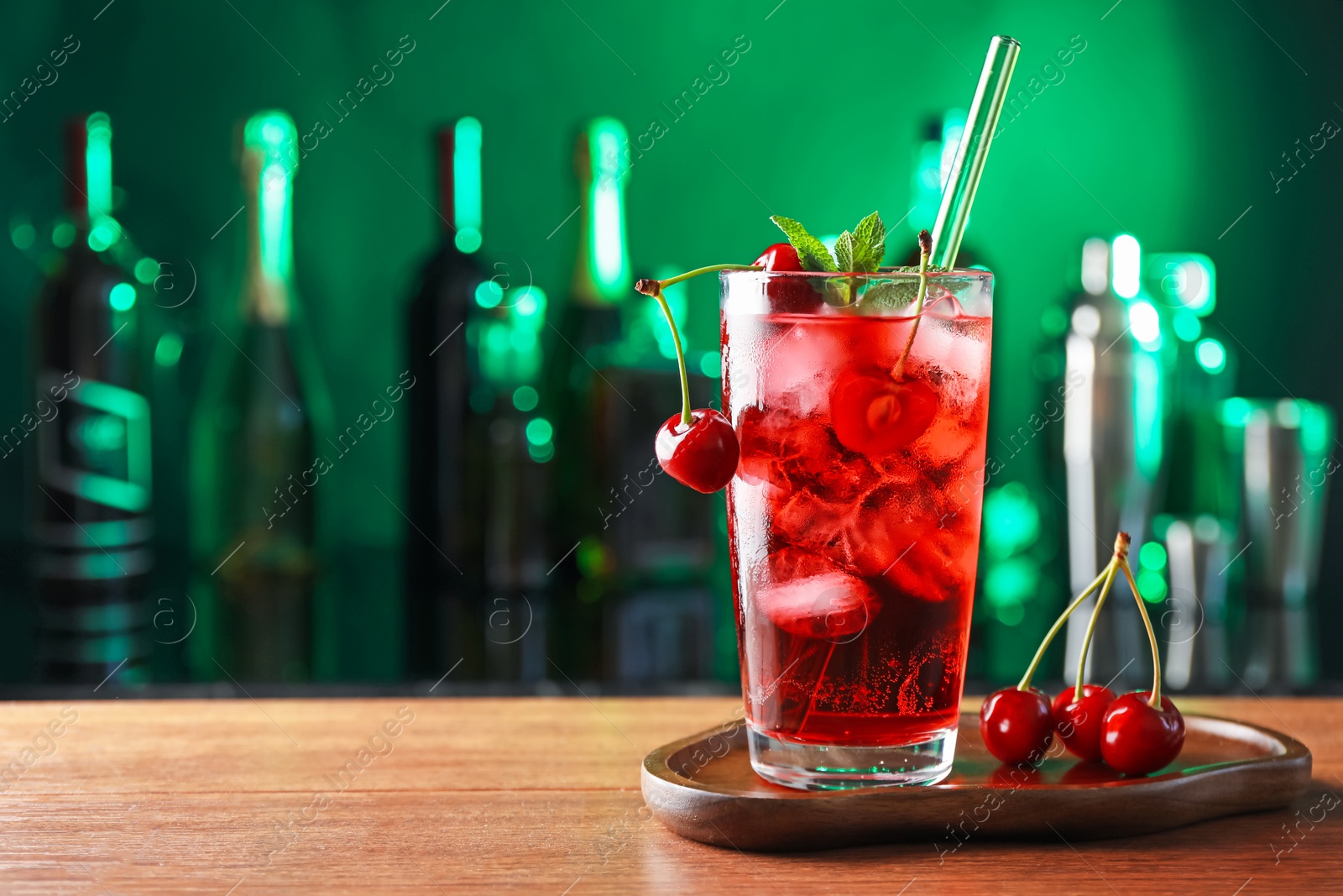 Tasty cherry soda water with ice cubes, berries and mint in glass on table against blurred green background, space for text Photo of Tasty cherry soda water with ice cubes, berries and mint in glass on table against blurred green background, space for text