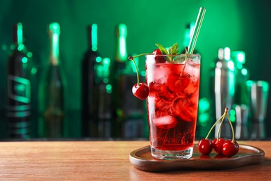 Photo of Tasty cherry soda water with ice cubes, berries and mint in glass on table against blurred green background, space for text