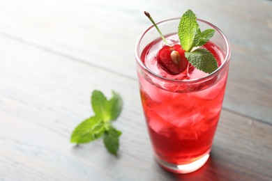 Photo of Tasty cherry soda water with ice cubes, berry and mint in glass on light table, closeup. Space for text